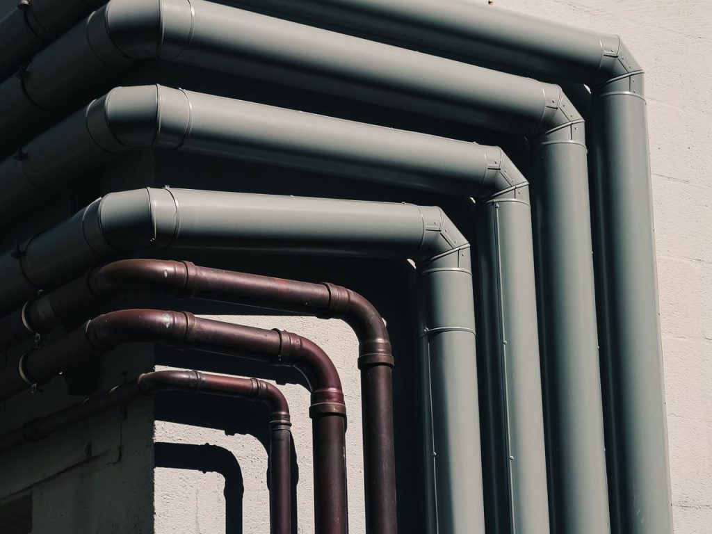 Close-up of industrial pipes forming a pattern on a buildings exterior wall, shot outdoors.